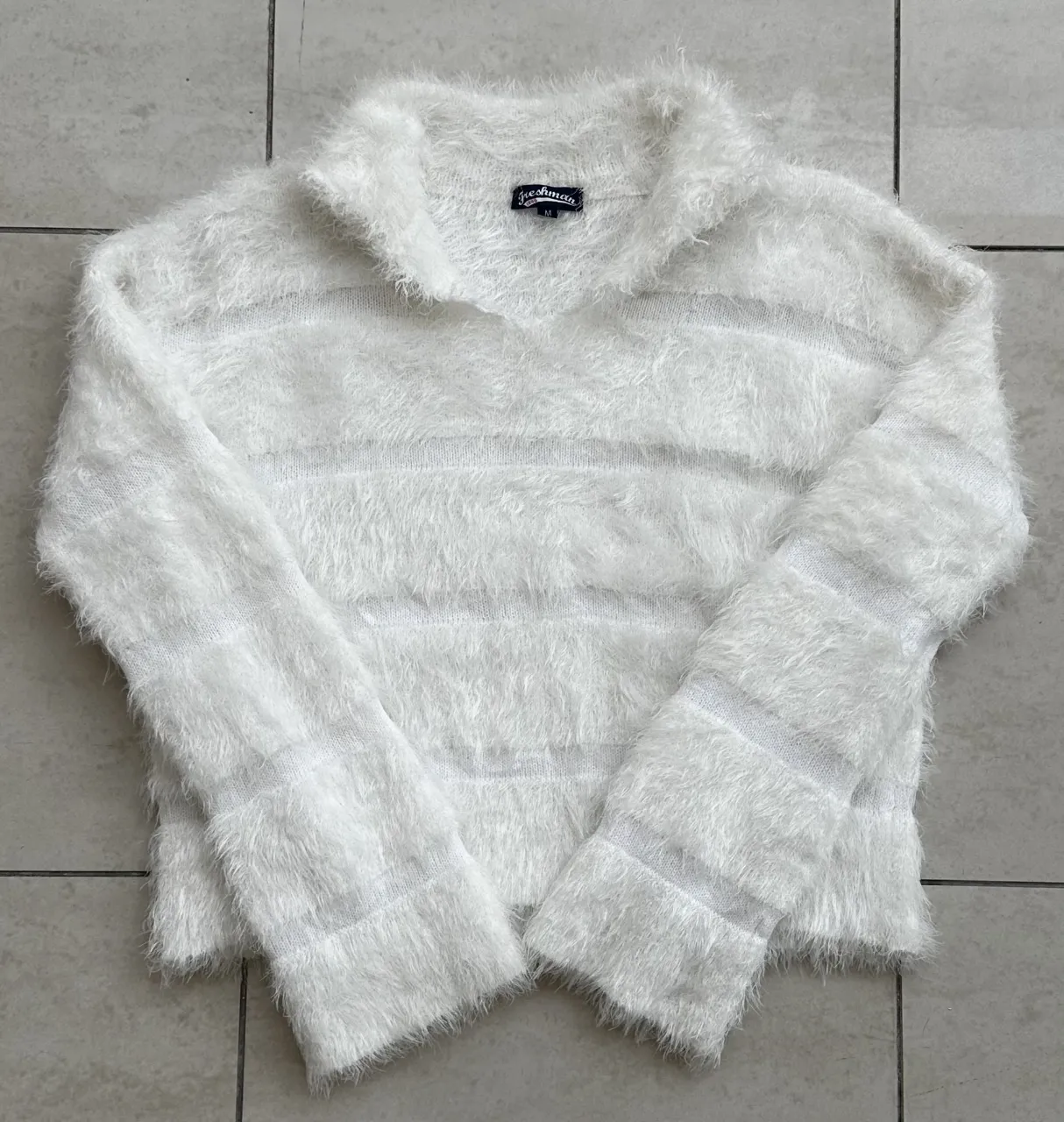 Sweater blanco con cuello escote en V y mangas largas. Posee detalles de franjas horizontales en relieve y textura de pelo.