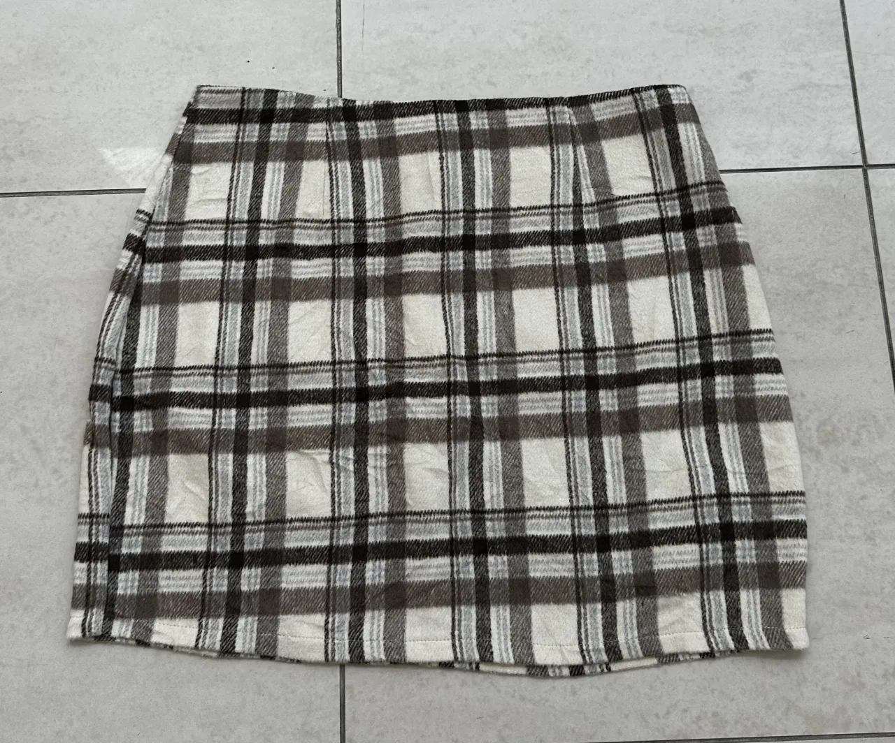 Pollera corta a cuadros escoceses en tonos blanco, marrón y negro. Posee cierre en la parte trasera.
