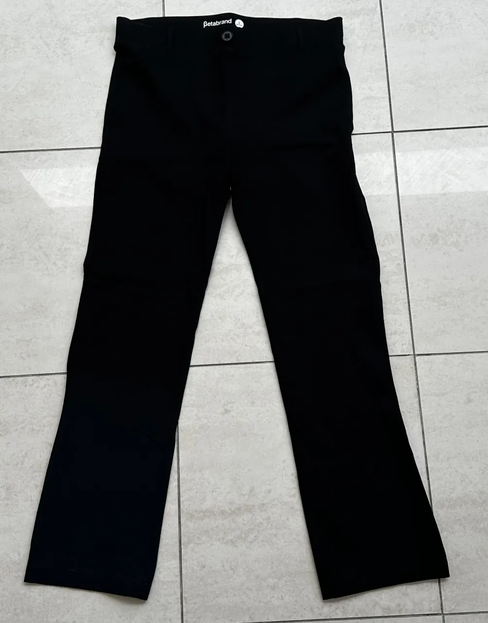 Pantalón negro liso con un botón en la cintura.