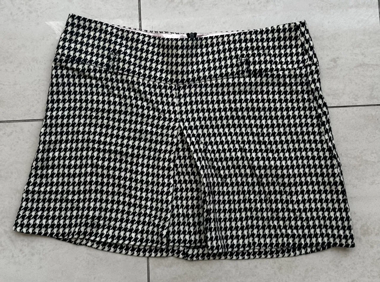 Pollera corta con estampado "pied de poule" en blanco y negro. Posee dos bolsillos delanteros y cierre en la espalda.