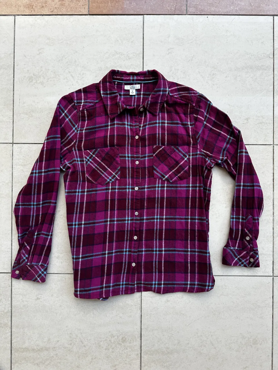 Camisa a cuadros de manga larga con botones al frente y dos bolsillos en el pecho. Cuello clásico.