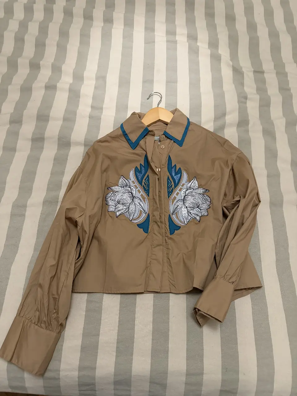 Camisa de mujer color marrón con detalles bordados en blanco y azul. Cuello y puños en azul. Marca: Justa Petra. Talle 2.