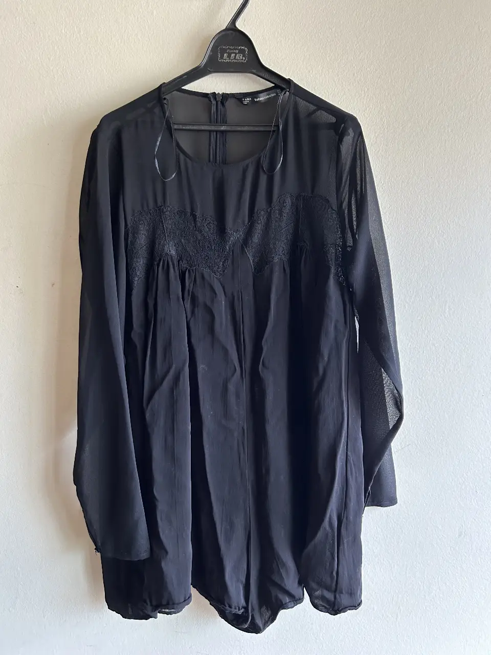 Mono negro de gasa con detalles de encaje en el frente. Manga larga y corte holgado. Ideal para un look elegante y sofisticado.