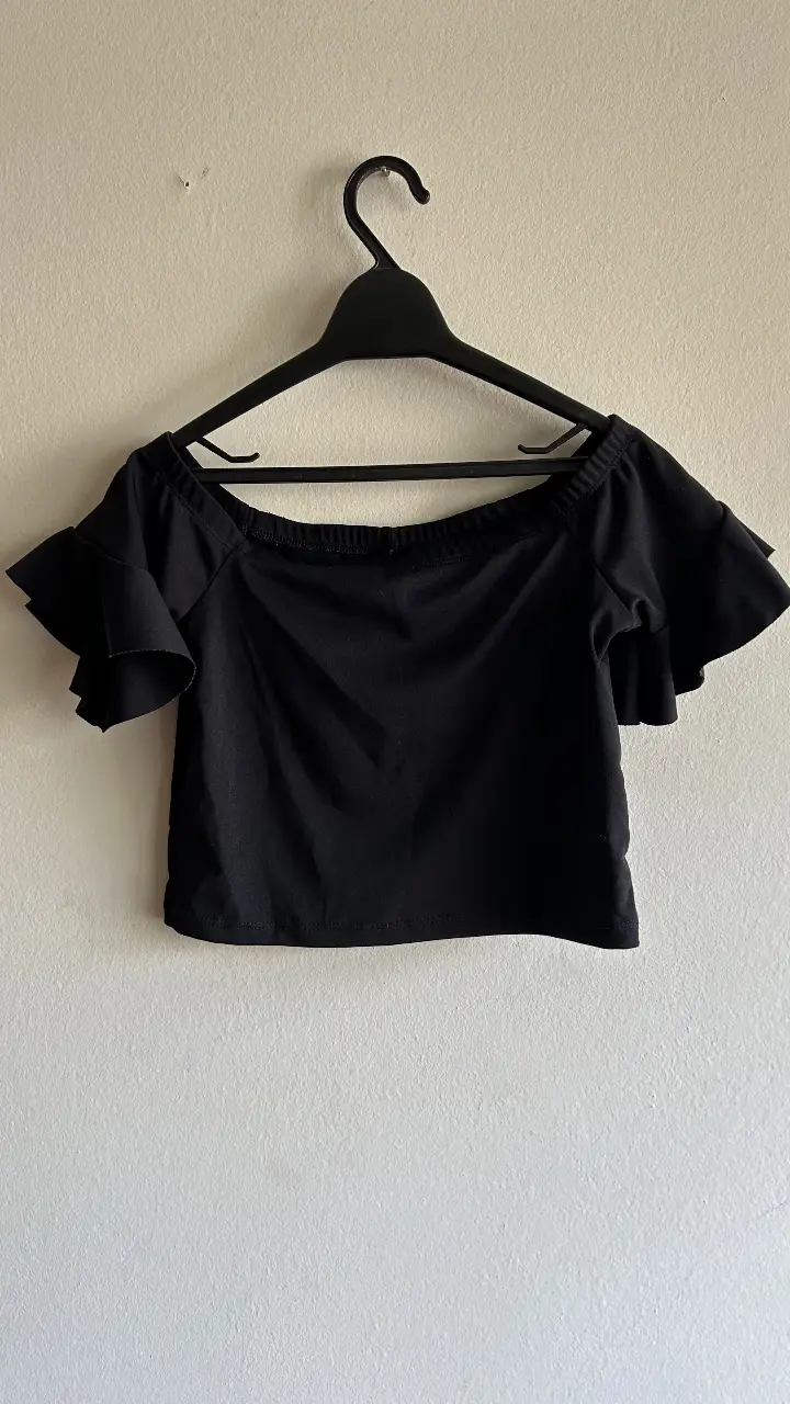 Top negro con mangas cortas con volados, ideal para un look casual y fresco. Perfecto para combinar con jeans o faldas.