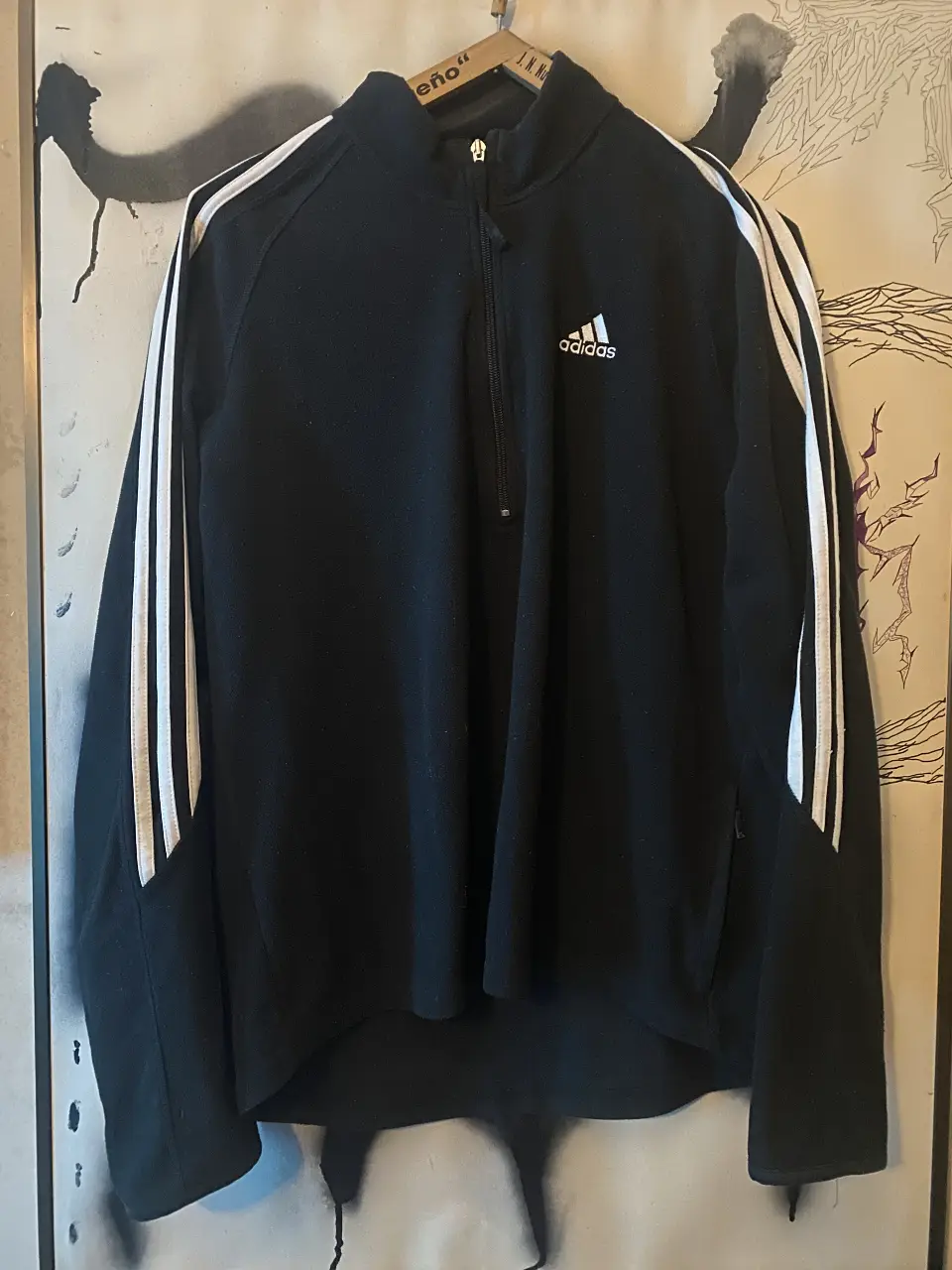 Buzo deportivo Adidas negro con cierre y detalles blancos en las mangas. Ideal para entrenar o usar en el día a día.