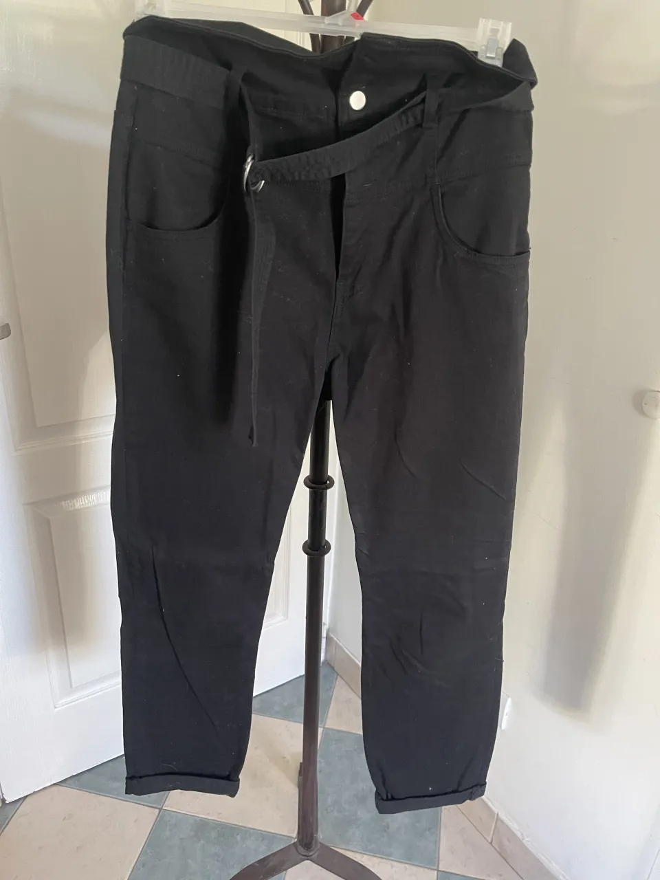 Pantalón negro con cinturón de tela. es tiro alto y se puede usar diblando un poco la cintura para afuera. Tiene bolsillos delanteros y traseros. 