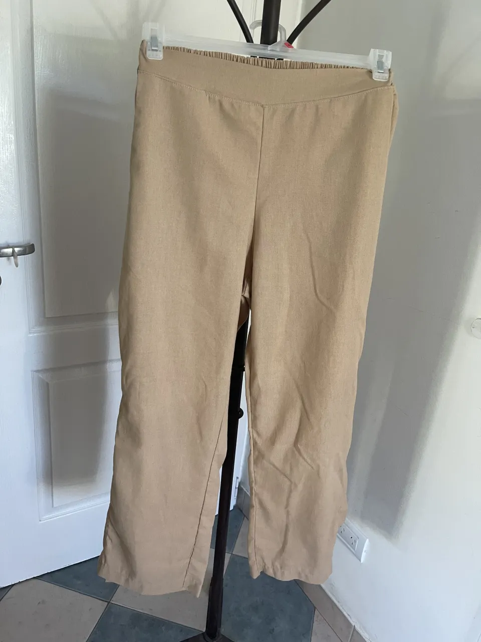 Pantalón de color beige con cintura elastizada y bolsillos laterales. Posee tajos en los bajos. tela tipo lino. con bolsillos de costado. cintura sin estirar 36cm estirando 39cm tiro 32 cm. largo 100