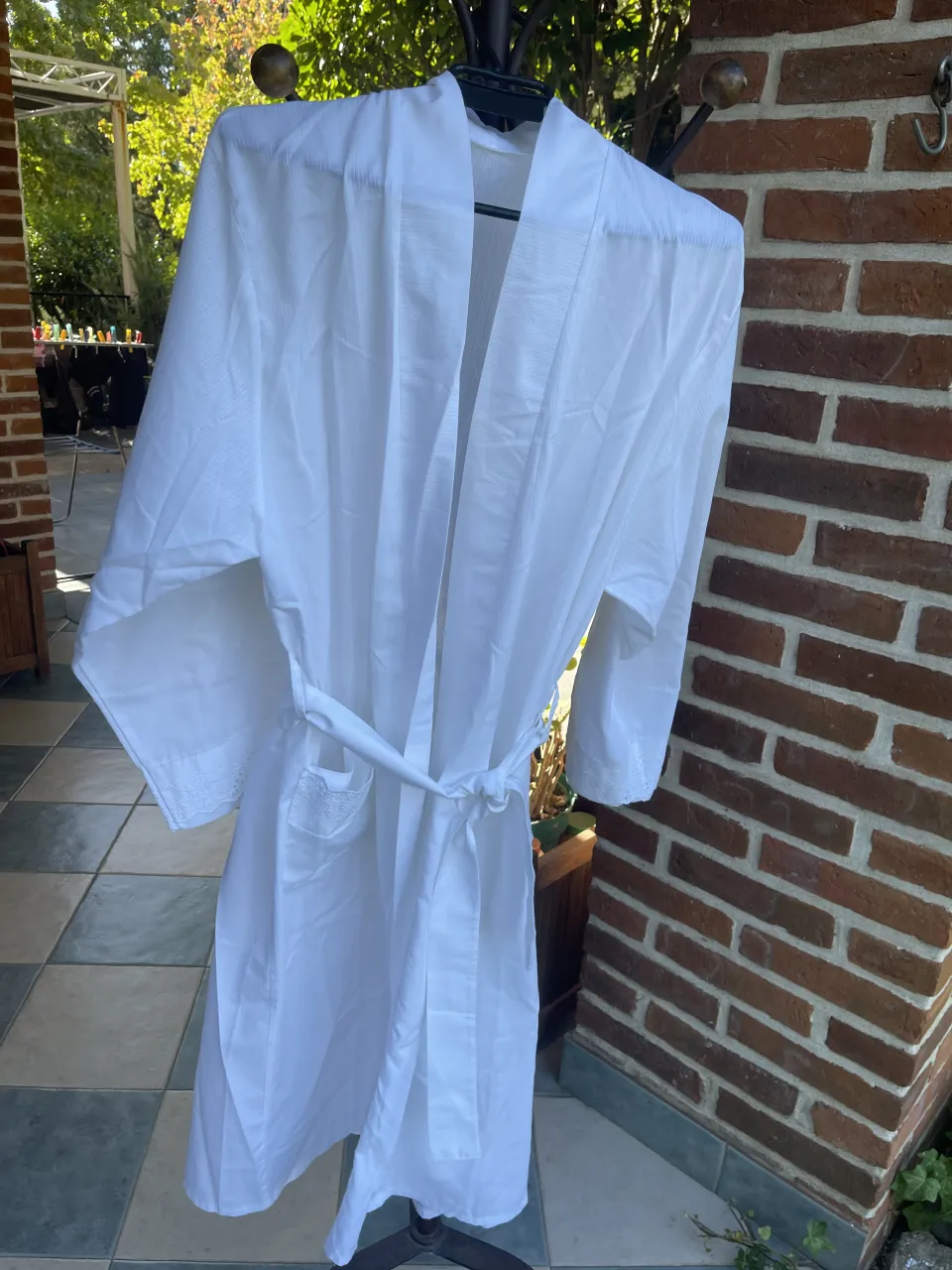 Bata blanca con cinturón del mismo material. Posee bolsillos en la parte delantera. con detalles de encaje en mangas y bolsillos