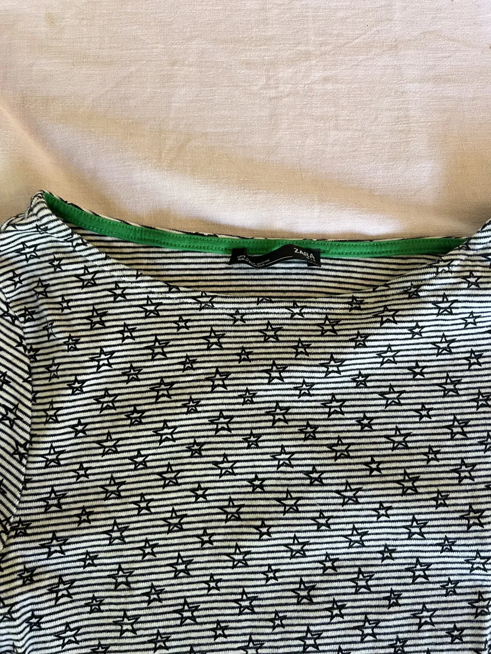 Remera de manga larga con estampa de estrellas y rayas horizontales. Cuello redondo con borde verde.