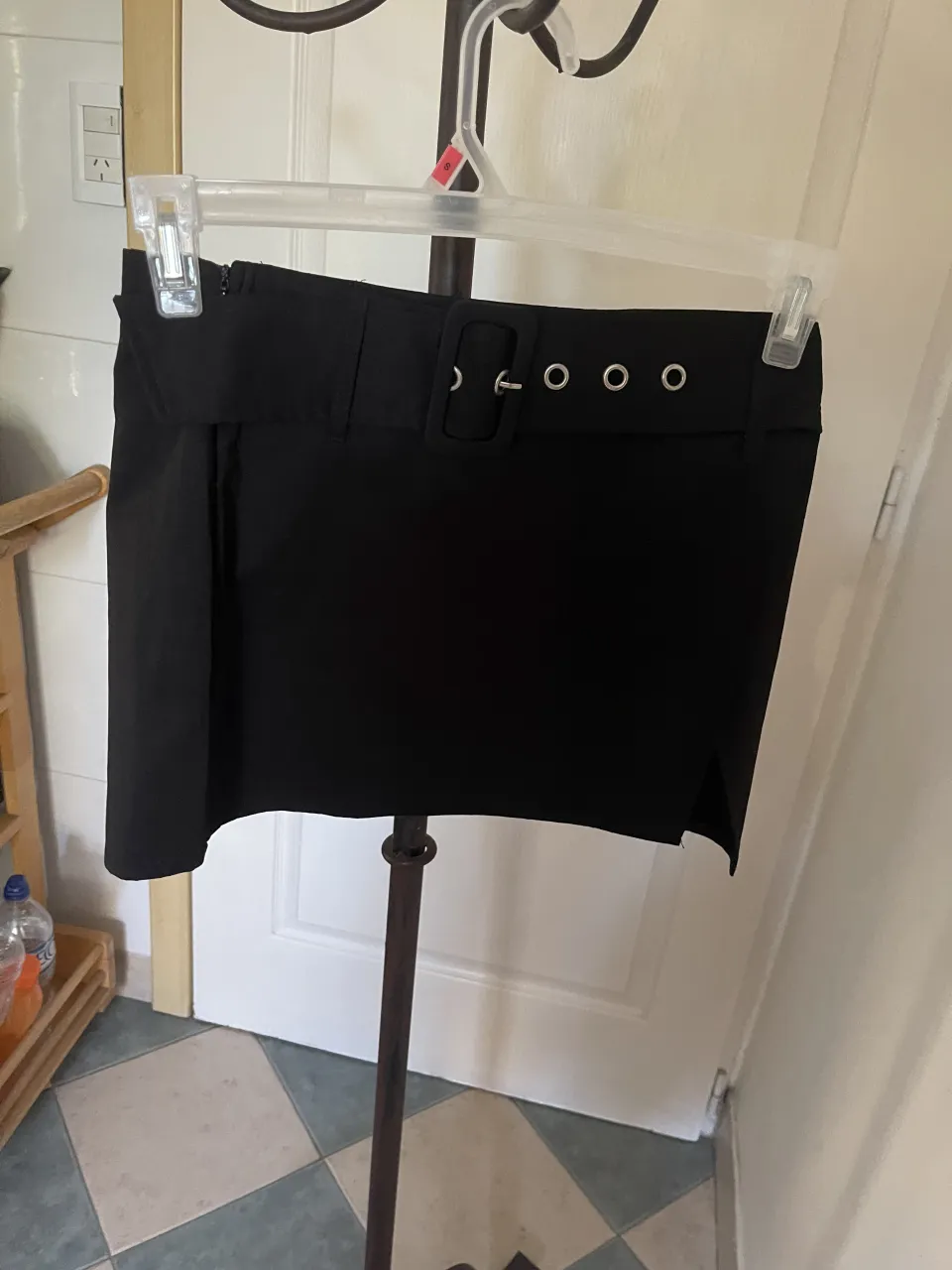 Pollera negra corta con detalle de hebilla y ojales en la cintura. Cierre lateral. y tajo lateral. cintura 36 cm largo 33 cm cadera 44