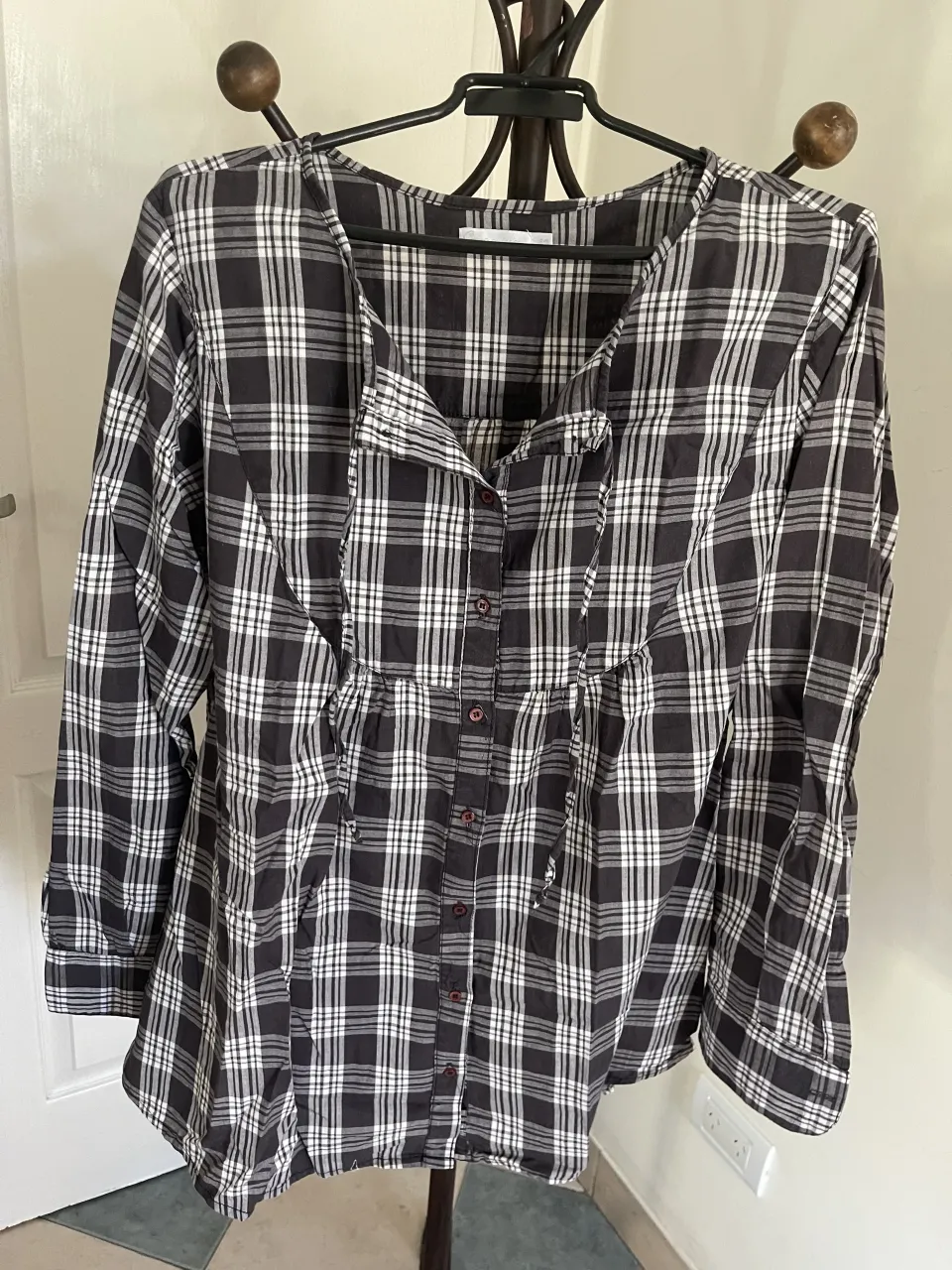 Camisa a cuadros de manga larga con botones al frente y detalle de lazo en el cuello. Posee un corte con frunces en la cintura. 