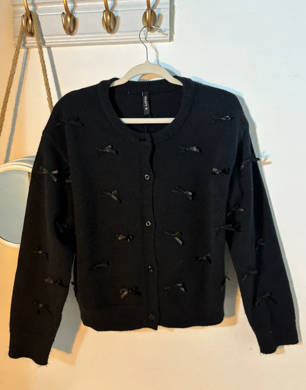 Cardigan negro de tejido suave con detalles de moños. Ideal para un look elegante y femenino. Perfecto para usar en cualquier ocasión.