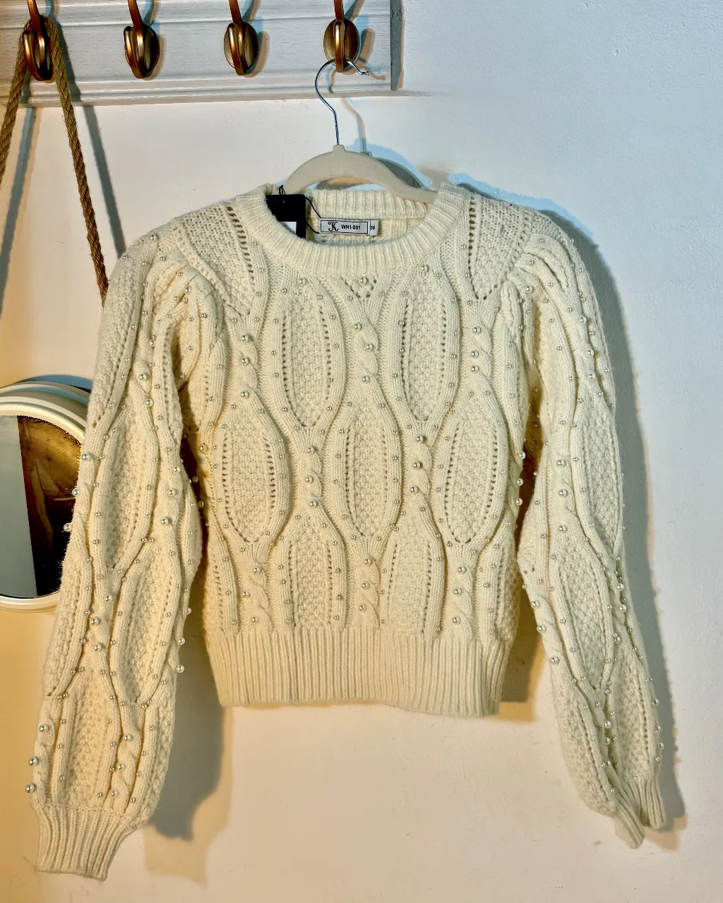 Sweater de mujer color crudo con detalles de perlas. Tejido con diseño de rombos y mangas abullonadas. Ideal para un look elegante y abrigado.