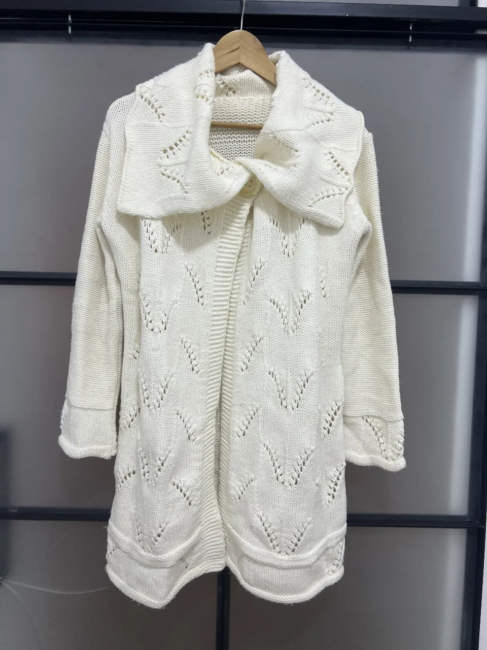 Cardigan largo de tejido grueso en color blanco, con cuello solapa y detalle calado en el frente. Ideal para un look casual y abrigado.