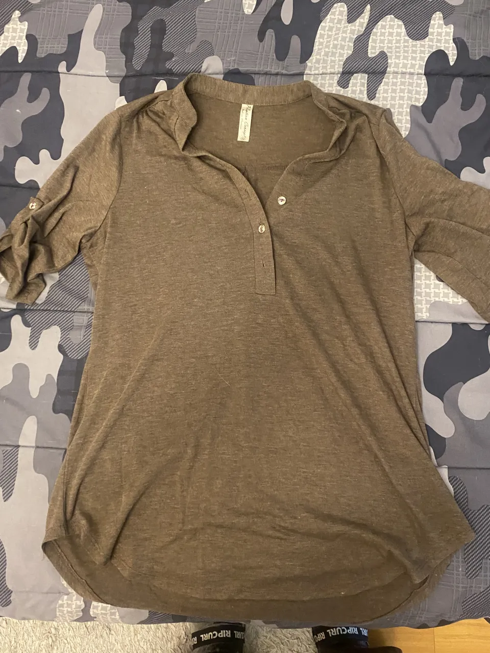 Remera manga larga de color marrón. Posee cuello escote en V con botones y puños con detalle de doblez.