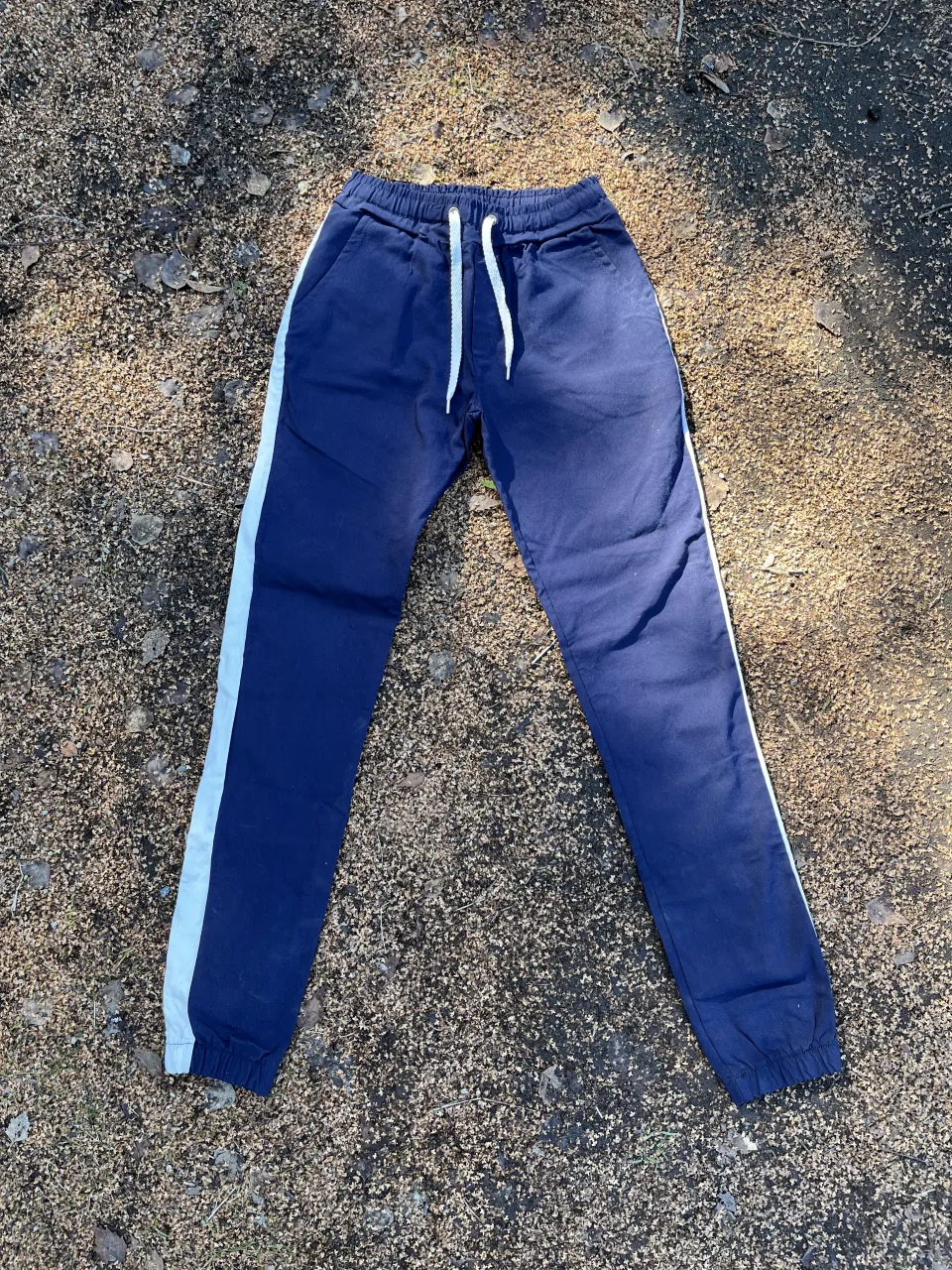 Pantalon de jogging azul marino con franjas laterales blancas. Cintura elastizada con cordón ajustable y puños en los tobillos. Ideal para un look deportivo y cómodo. Talle 16
