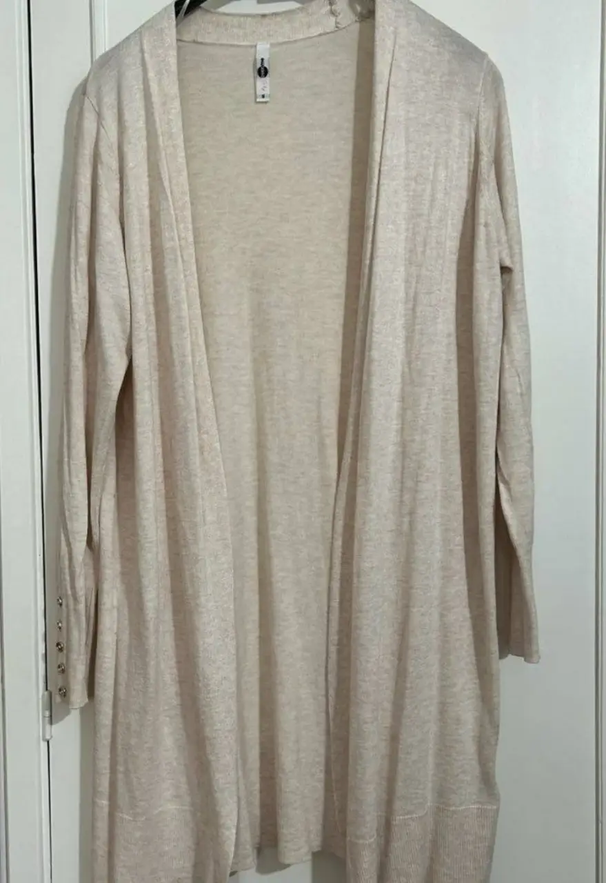 Cardigan largo de tejido liviano en color crudo, ideal para usar en cualquier ocasión. Posee mangas largas con detalles de botones en los puños.