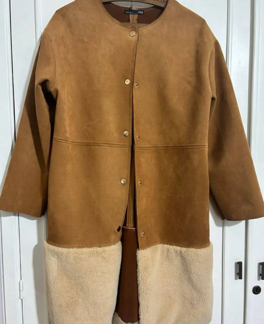 Tapado largo de gamuza marrón con detalles de piel en la parte inferior. Ideal para el invierno, con un diseño elegante y abrigado.