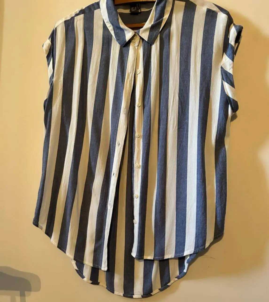 Camisa a rayas verticales en blanco y azul, con cuello y botones. Ideal para un look casual y fresco.
