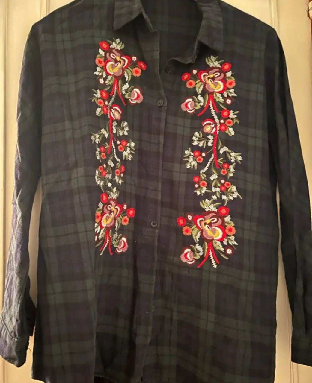 Camisa a cuadros en tonos oscuros con bordados florales en la parte delantera. Ideal para un look casual con un toque de estilo.