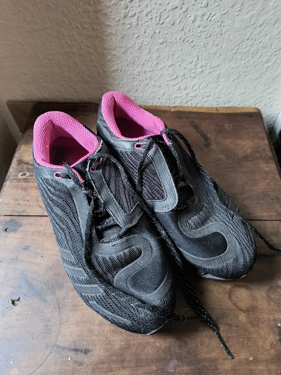 Zapatillas Adidas negras con detalles en rosa, ideales para running o entrenamiento. Diseño moderno y cómodo.