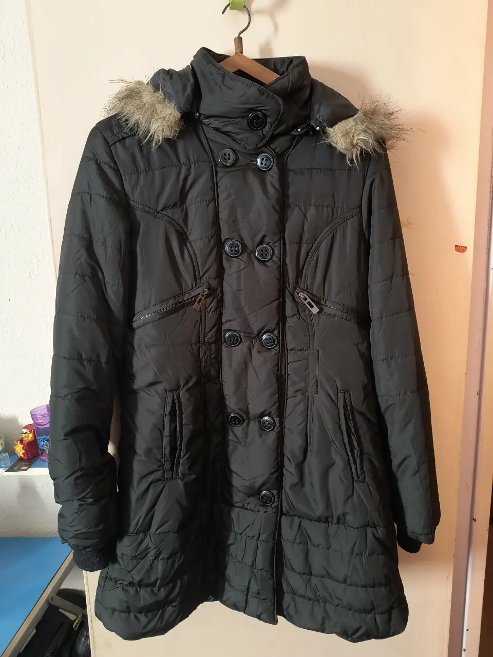 Campera negra acolchada con capucha y detalles de piel sintética. Posee cierre y botones, ideal para el invierno.