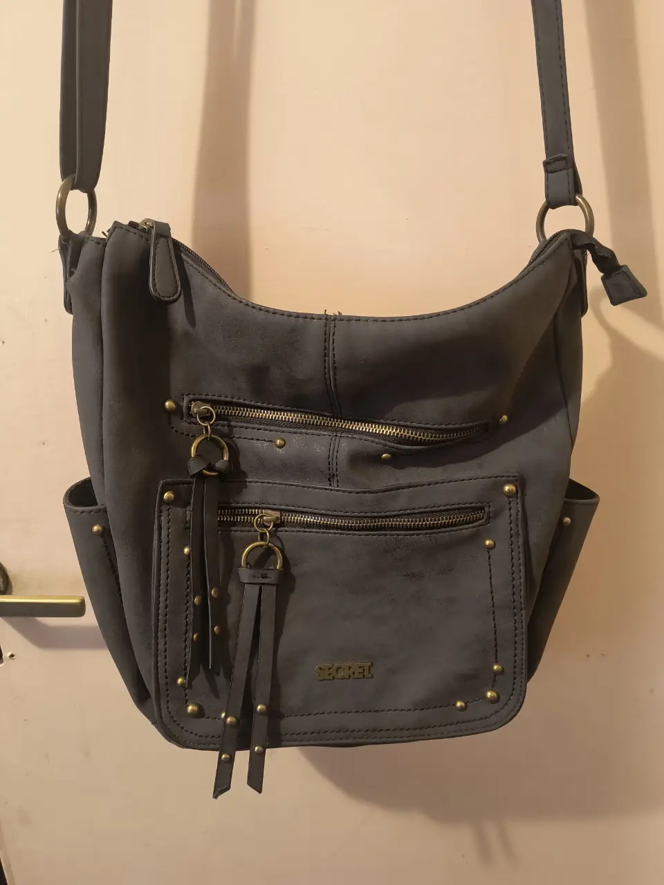 Cartera bandolera gris Secret, con múltiples bolsillos y detalles dorados. Ideal para un look casual y funcional.