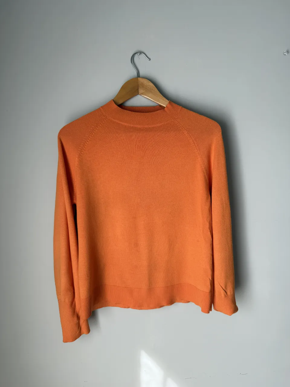 Sweater naranja de cuello redondo y manga larga. Presenta un pequeño detalle de rotura en la parte superior trasera del cuello.