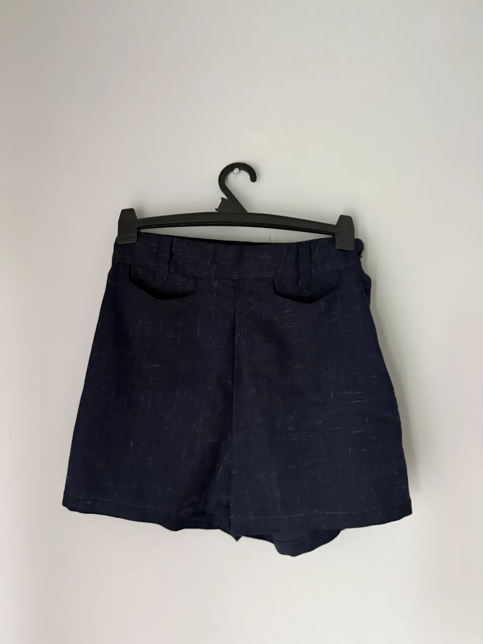 Shorts de lino azul oscuro, tiro alto, con bolsillos y un diseño sutil en la tela. 