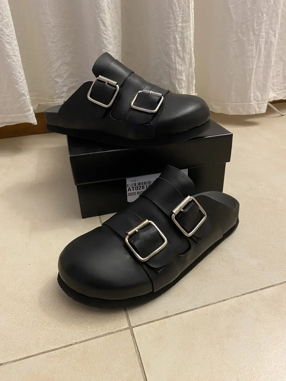 Zuecos negros de cuero con hebillas plateadas. Ideales para un look casual y moderno. Tiene detalle en hebilla