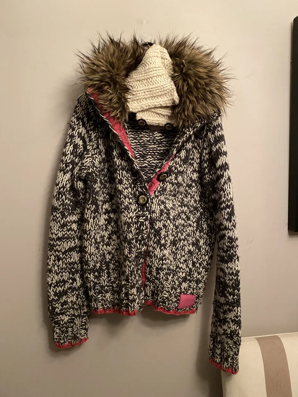 Sweater tejido con capucha de pelo sintético. Posee botones al frente y detalles en color rosa.