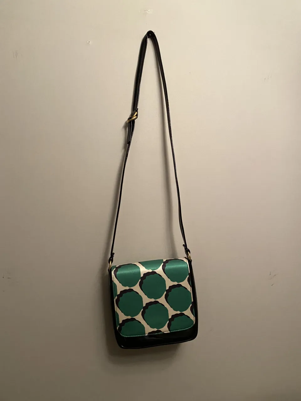 Cartera negra con solapa estampada con círculos verdes y detalles blancos. Correa larga ajustable.