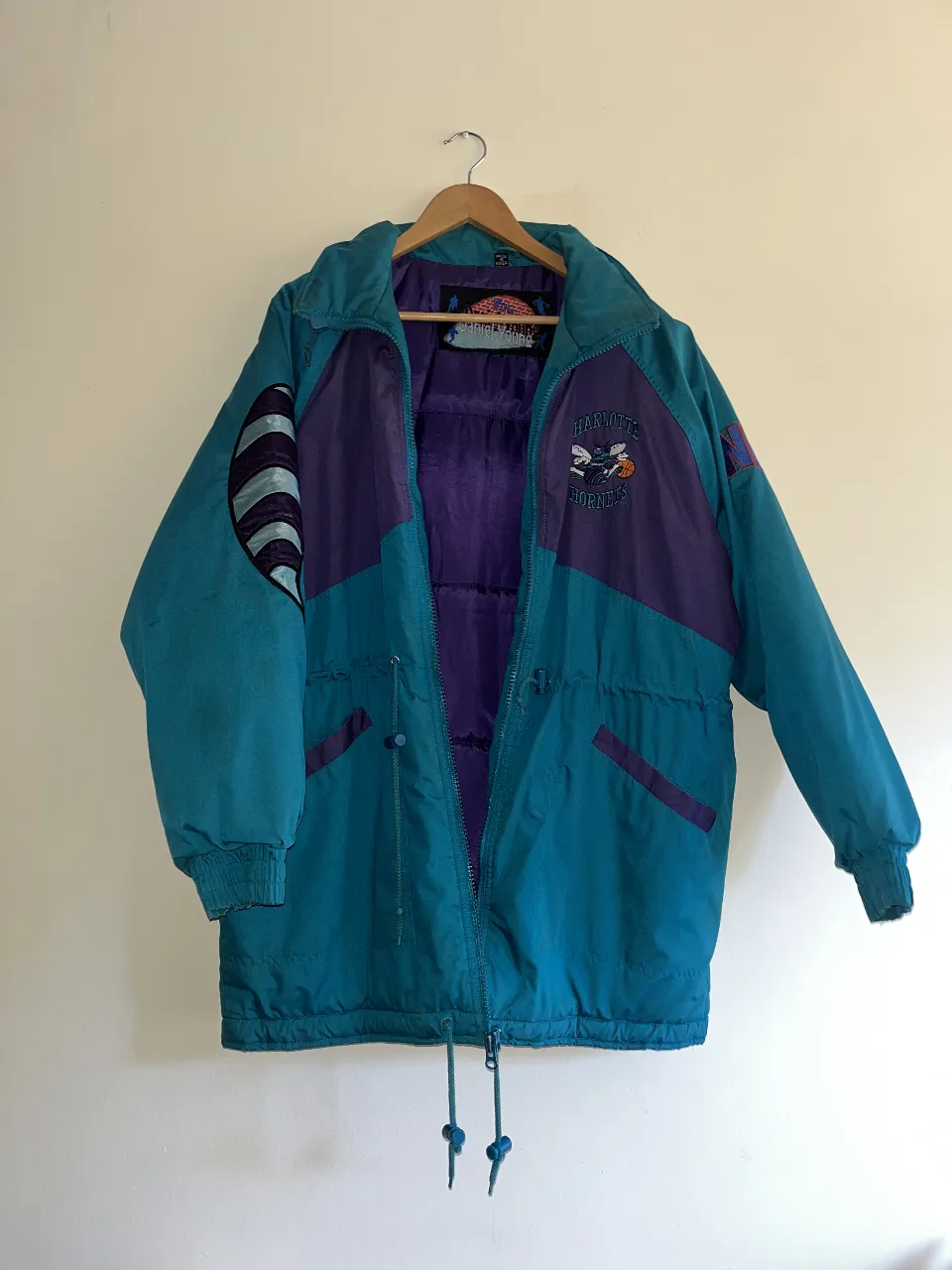 Campera deportiva vintage de los Charlotte Hornets, con diseño retro en tonos turquesa y violeta. Ideal para fanáticos del básquet y amantes del estilo urbano.
