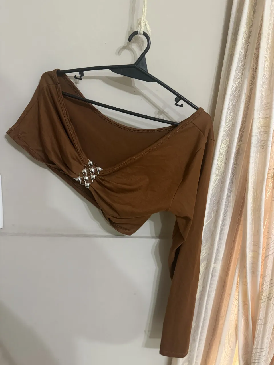 Top una manga larga de color marrón. Posee un detalle de strass plateado en la parte delantera.