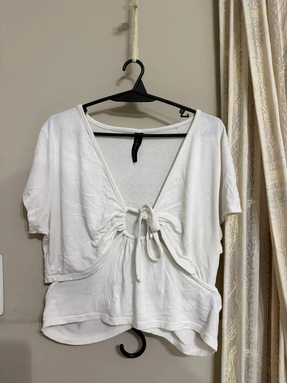 Remera blanca de manga corta con escote pronunciado y detalle de lazo anudado en el frente. Posee un recorte en la cintura.