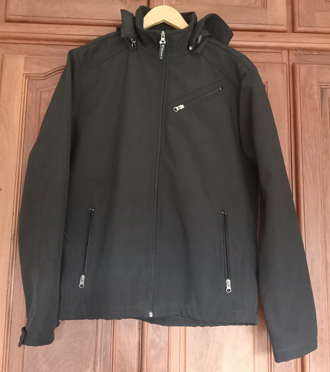 Campera negra con capucha, cierre completo y bolsillos frontales con cierre. Tiene un bolsillo superior diagonal con cierre.