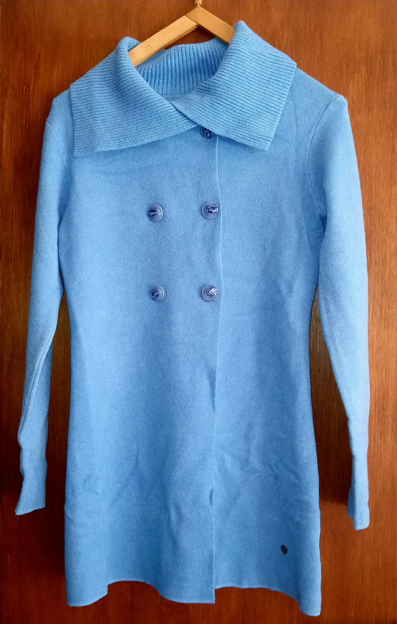 Cardigan largo de tejido color celeste, con cuello solapa y doble hilera de botones al frente. Posee dos bolsillos inferiores.