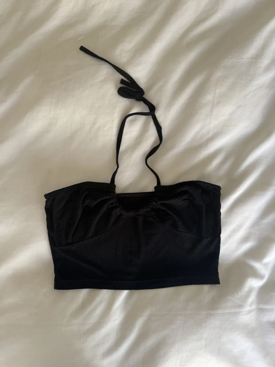 Top negro con tiras para atar en el cuello. Posee detalles de frunces en la parte superior y tela acanalada.