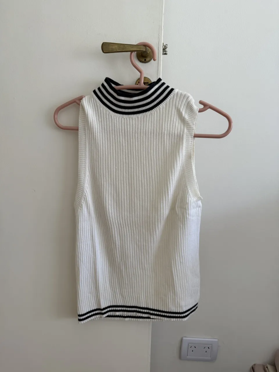 Sweater musculosa blanco de tejido acanalado con cuello alto y detalles de rayas negras en el cuello y en el borde inferior.