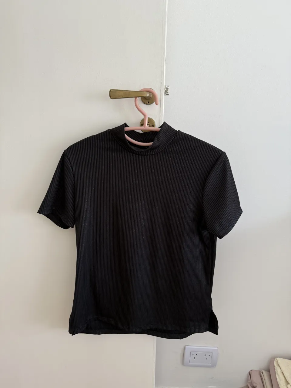 Remera negra de manga corta y cuello alto. Posee una textura acanalada. La tela tiene brillitos