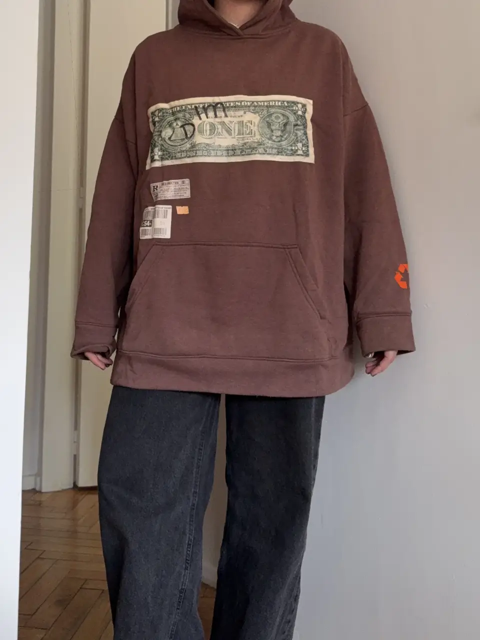 Buzo canguro marrón con estampado de billete de dólar en el frente y logo @JGGRMKT en la espalda. Estilo streetwear, ideal para un look casual y cómodo.