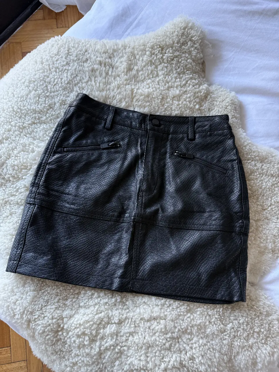 Minifalda de cuero sintético con textura de reptil. Posee bolsillos delanteros con cierre y dos bolsillos traseros. Ideal para un look moderno y audaz.