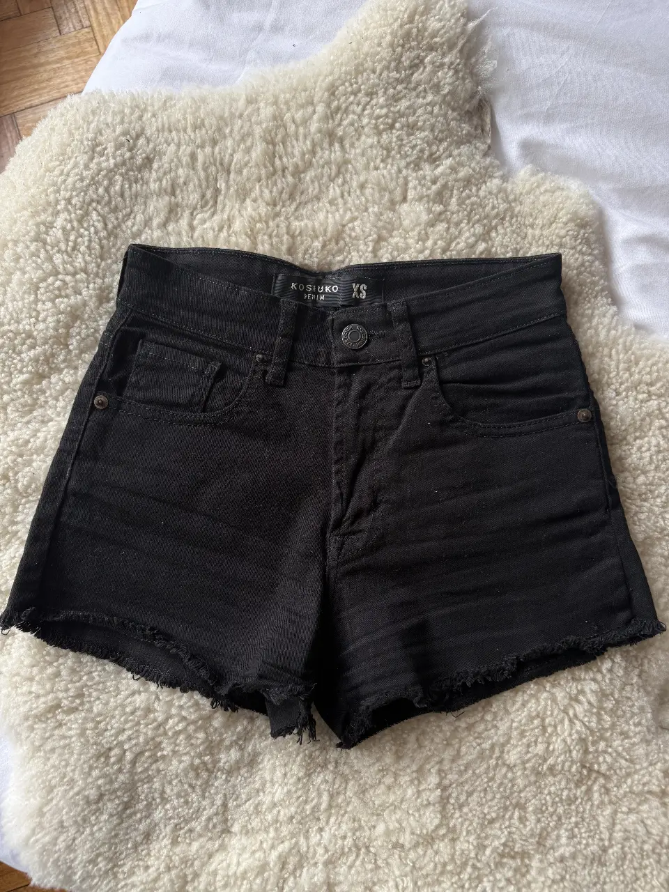 Short de jean negro de mujer, tiro alto, al cuerpo, con detalles desflecados en el borde. Marca Kosiuko, talle XS.