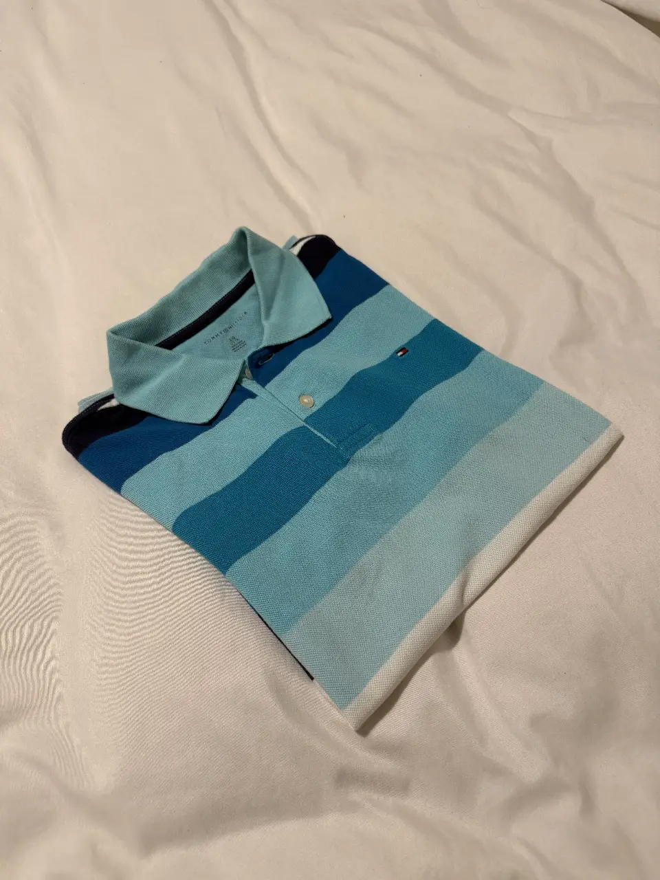 Chomba polo Tommy Hilfiger a rayas horizontales en tonos azules y celeste. Cuello y mangas en azul marino. Logo bordado en el pecho. TALLE PARA NIÑOS DE 12 A 14 AÑOS
