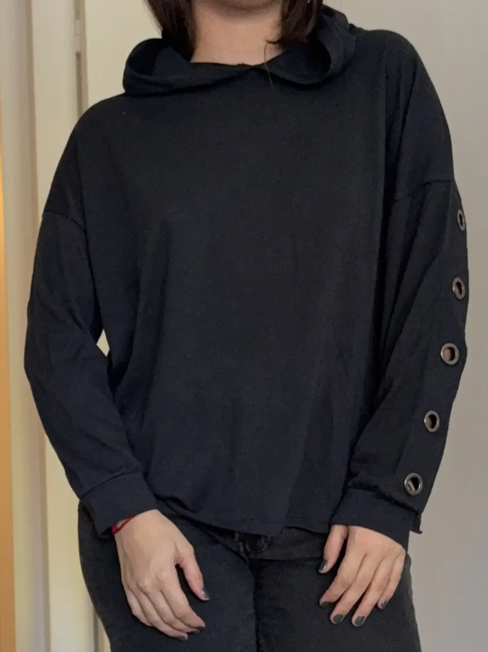 Buzo negro con capucha y mangas largas. Detalles de ojales metálicos en las mangas. Ideal para un look casual y moderno.