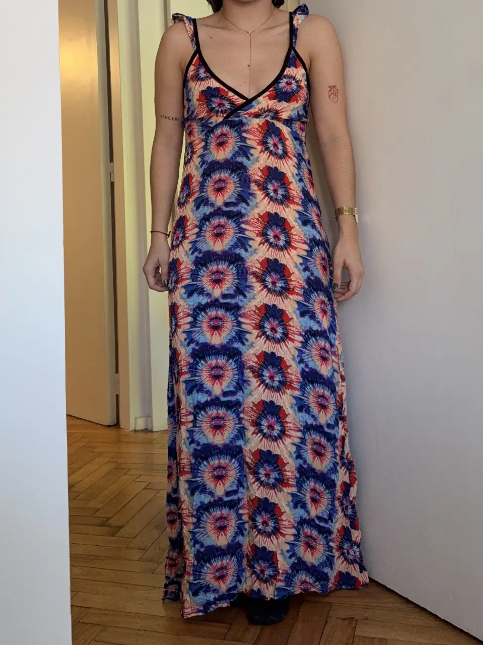 Vestido largo de mujer, con estampado floral en tonos azules, rojos y amarillos. Tiene tirantes finos y un escote en V con detalles en negro. Ideal para un look fresco y veraniego.