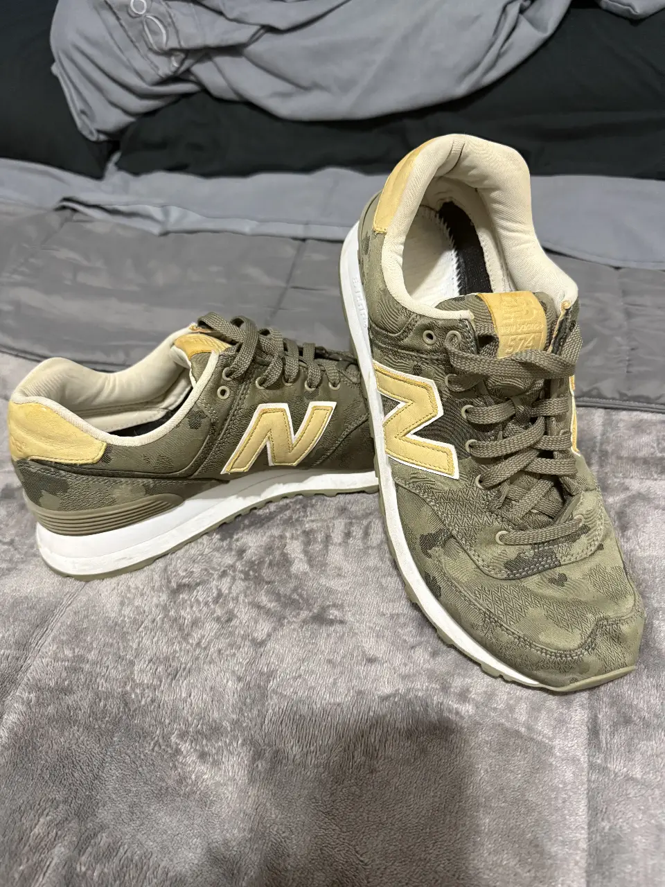 Zapatillas New Balance 574 con estampado camuflado en tonos verdes y detalles amarillos. Ideales para un look casual y urbano.
