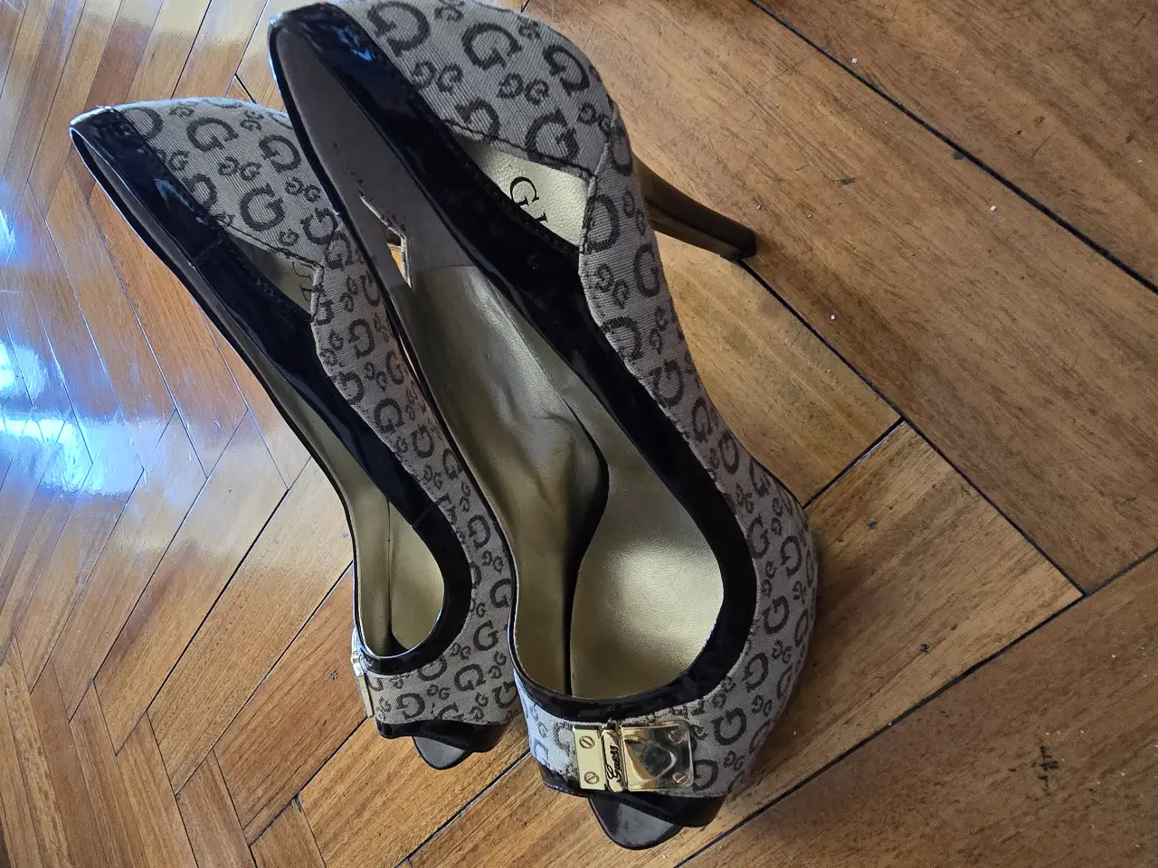 Elegantes tacos Guess con estampado del logo de la marca. Diseño peep toe con detalles en charol negro y hebilla dorada. Ideales para eventos formales o fiestas.