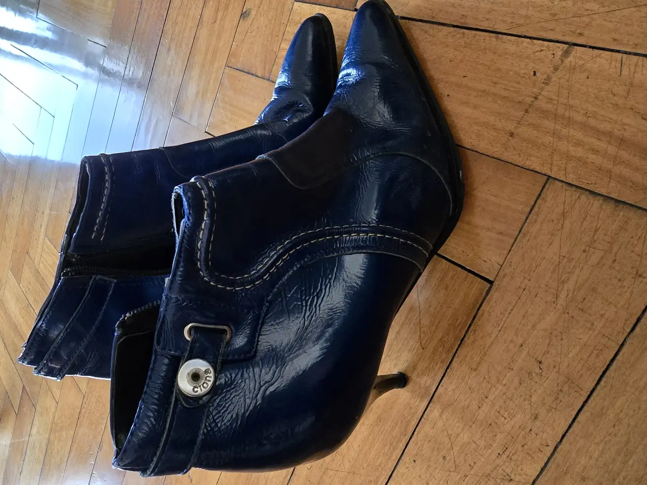 Botines de cuero charol azul, con taco fino y punta. Detalles de hebilla y cierre lateral. Ideales para un look elegante y sofisticado.