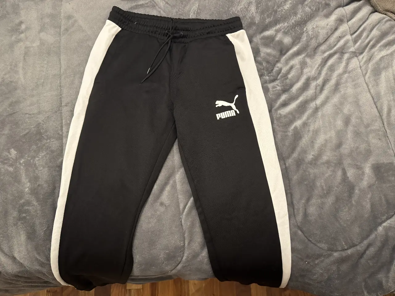 Pantalón deportivo Puma negro con franjas blancas laterales y logo de la marca. Ideal para un look casual y cómodo. 3364021617